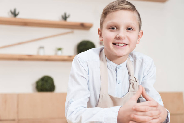 smiling boy in apron looking at camera while leaning on table at cafe  - Фото, зображення