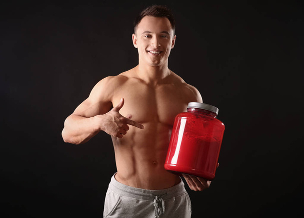 Sporty young man with jar of protein powder on black background - Fotografie, Obrázek