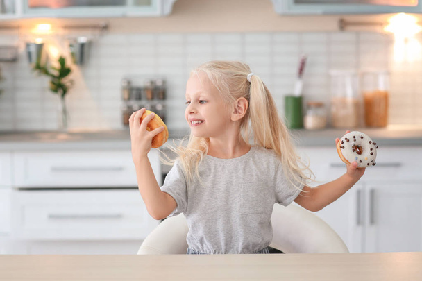 Little girl with sweet donuts at kitchen table - Foto, Imagem