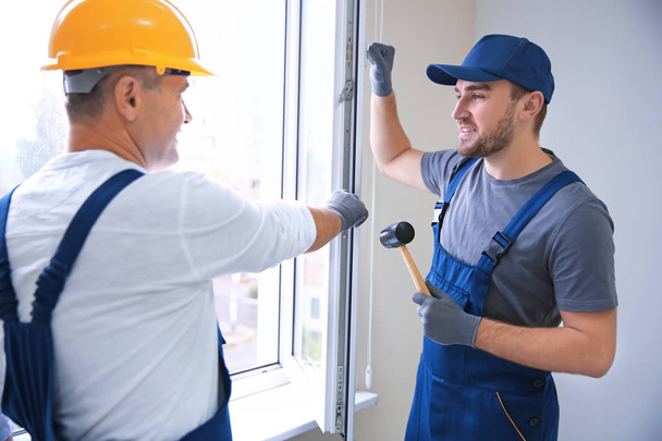Construction worker with trainee installing window in house - 写真・画像