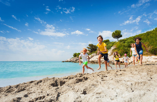 Large group of boys and girls with kids running on the beach near sea water on sunny hot day - Foto, imagen