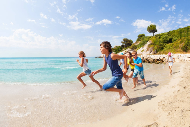 Group of active kids having a race on sandy Mediterranean beach in summertime - 写真・画像