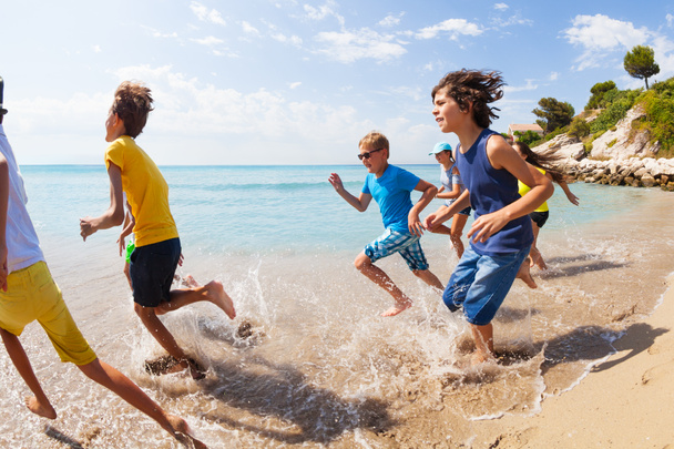 Grote groep kinderen lopen op het strand aan de rand van het water op hete vakantie zomerdag - Foto, afbeelding