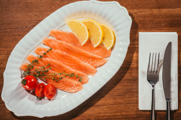 κόκκινο κομμένο σε φέτες ψάρι στο πιάτο με ΝΤΟΜΑΤΕΣ και δαχτυλίδια πορτοκάλι πάνω από την ξύλινη επιφάνεια  - Φωτογραφία, εικόνα