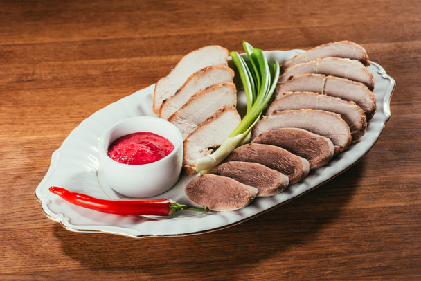 Çeşitli et dilimleri ile sosu, yeşil soğan ve biber ahşap masa üzerinde beyaz tabakta servis - Fotoğraf, Görsel