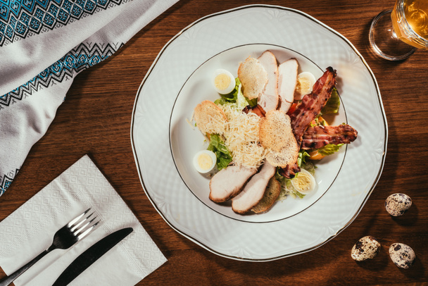 vista de las lonchas de jamón con carne frita y algunos huevos cocidos en el plato sobre la mesa con tenedor y cuchillo en la servilleta
  - Foto, Imagen