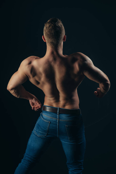 Sportsman show muscles on dark background - Foto, afbeelding