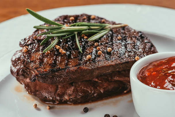 Nahaufnahme von gegrilltem Steak mit Pfeffer, Rosmarin und Soße auf weißem Teller - Foto, Bild
