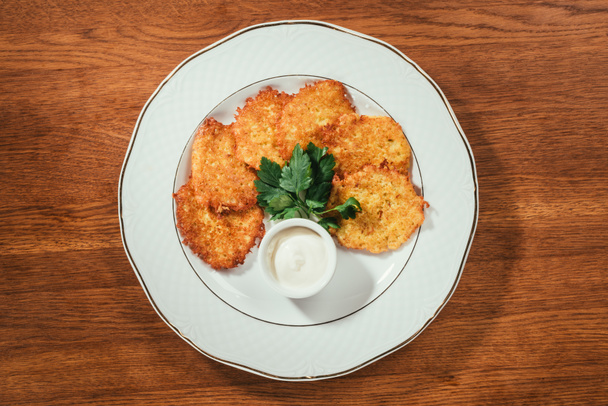 Top view of potato pancakes served with sour-cream sauce on plate on wooden table - Photo, Image