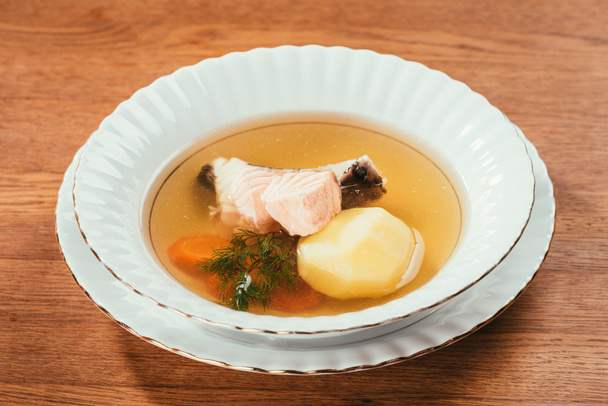 Hot soup with salmon and vegetables served in white plate on wooden table - Photo, Image