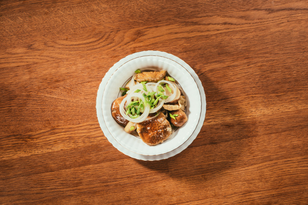 Top view of pickled mushrooms with onion on white plate on wooden table - Photo, Image
