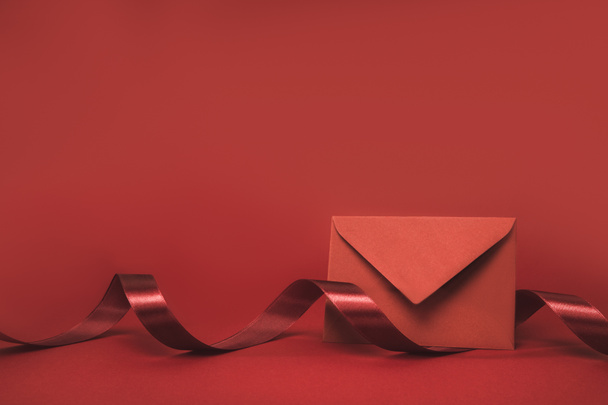 close up view of envelope and ribbon isolated on red - Foto, Imagen