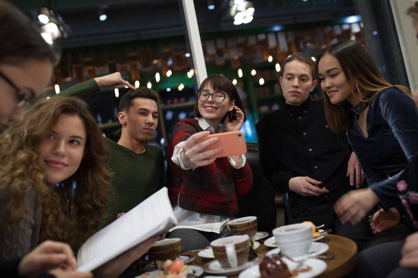 Group of positive teens use a smartphone and spend time in a cafe. - Фото, изображение