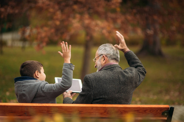 Grandpa and his grandson spend time together in the park. They are sitting on the bench. Walking in the park and rejoicing - Photo, Image