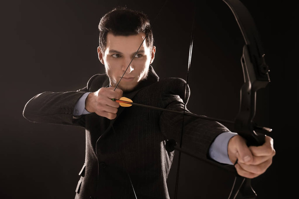 Young businessman practicing archery on dark background - Foto, afbeelding
