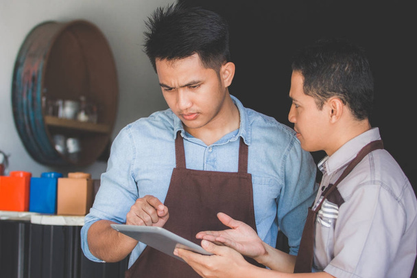 coffee shop owner discussing with his employee using tablet - 写真・画像