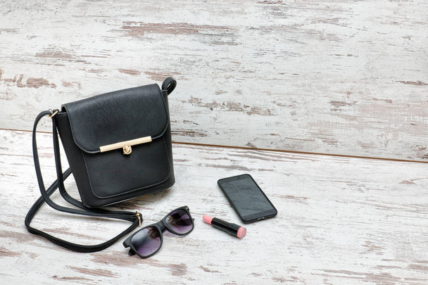 Kis fekete női táska, napszemüveg, rúzs és szúró telefon - Fotó, kép