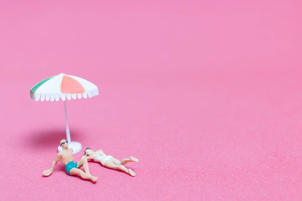 Miniature people wearing swimsuit relaxing on pink background  - Foto, imagen
