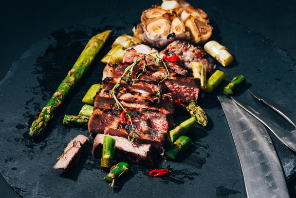 Крупный план вкусного сочного мяса на гриле со специями и спаржей на черном
 - Фото, изображение