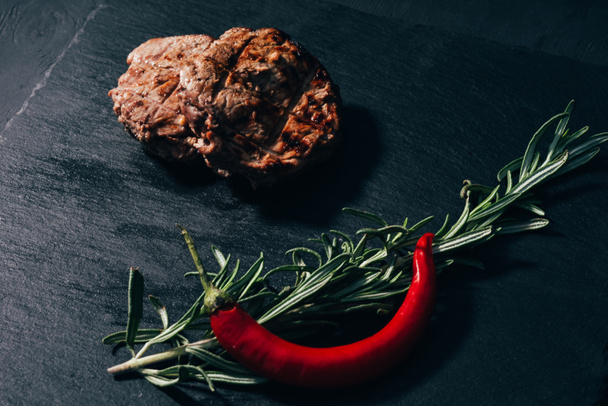 vergrote weergave van heerlijke gegrilde steak met rozemarijn en chili peper op zwart  - Foto, afbeelding