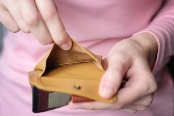 άδειο πορτοφόλι στα χέρια του μια νεαρή γυναίκα σε ένα ροζ πουλόβερ. - Φωτογραφία, εικόνα