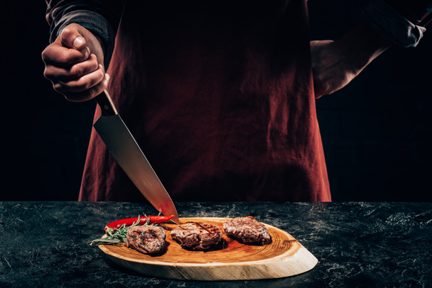 bıçak ve lezzetli ızgara biftek biberiye ve biber ahşap tahta üzerinde ile önlük daimi Şef kadeh kırpılmış - Fotoğraf, Görsel
