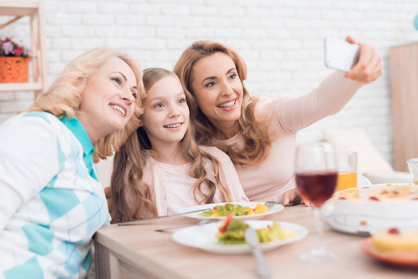 Mom, grandmother and granddaughter do selfie at the dinner table. They have dinner at home. They have vegetables and sweets on their table. - Valokuva, kuva