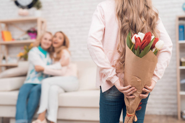 A little girl gives a bouquet of tulips to her mom and grandmother. They celebrate Mothers Day. They have a traditional family holiday. - Foto, afbeelding