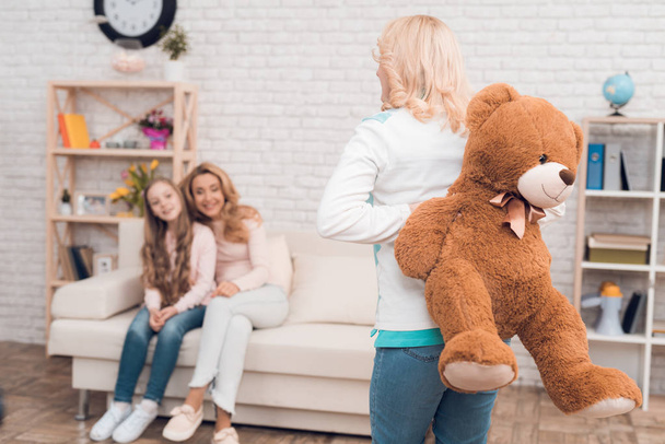 Mom and grandmother give a little girl a big toy bear. They make her a surprise. The family has dinner at home - they have a holiday. - Fotoğraf, Görsel