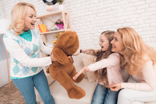 Mom and grandmother give a little girl a big toy bear. They make her a surprise. The family has dinner at home - they have a holiday. - Foto, Bild