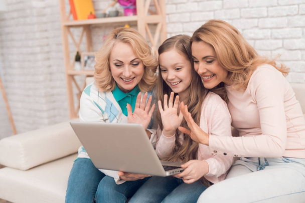 Mom, grandmother and girl are looking at something on the laptop screen. They are in a good mood. They are smiling. - Photo, image