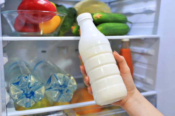 Woman taking bottle of milk from refrigerator, closeup - Photo, image
