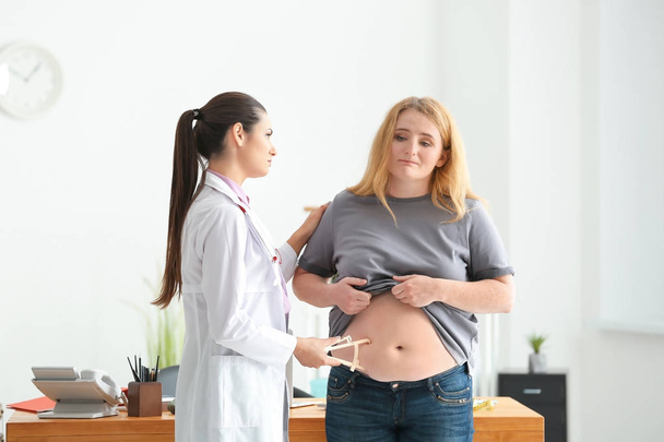 Jonge vrouwelijke arts meten vetlaag van overgewicht vrouw met remklauw in kliniek - Foto, afbeelding