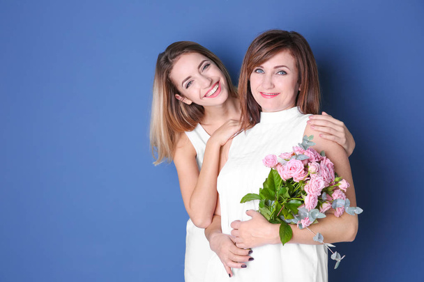 Attractive young woman with her mother in matching dresses on color background - Фото, изображение