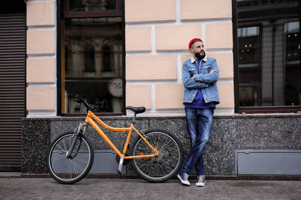 Attractive young hipster with bicycle on city street - Photo, Image