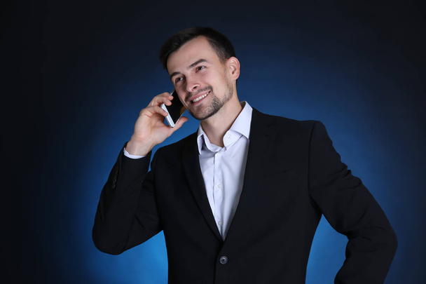 Man in formal suit talking on phone against dark background - Фото, изображение