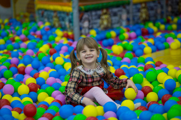 Bonne petite fille en robe rouge jouer dans la piscine avec des boules en plastique colorées. drôle enfant avoir amusant à l'intérieur
. - Photo, image