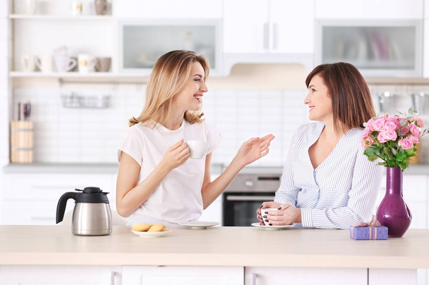 Attractive young woman drinking coffee with her mother at home - Foto, imagen