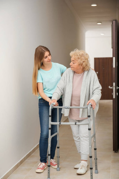 Young woman and her elderly grandmother with walking frame in corridor - Foto, Imagen