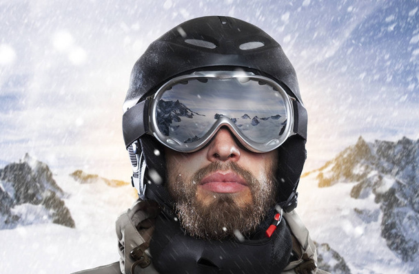 portrait of a snowboarder with helmet and goggles in front of sunrise in wintry mountains landscape while a stormy blizzard - Фото, изображение
