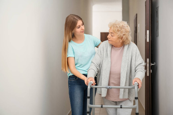 Young woman and her elderly grandmother with walking frame in corridor - Foto, immagini