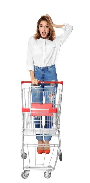 Young woman with empty shopping cart on white background - Valokuva, kuva