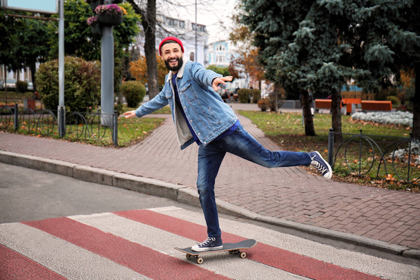 Attractive young hipster riding skateboard on city street - Foto, afbeelding