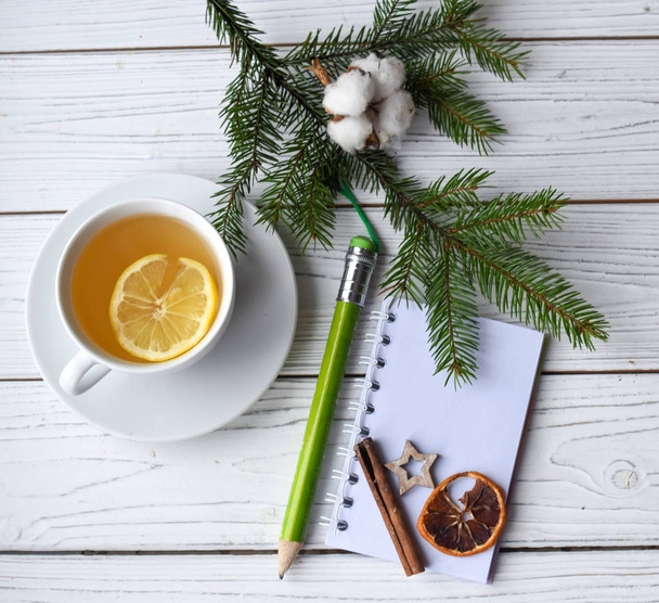 A festive winter mock up photo with a cup of tea, fir twigs, an opened note book, a pencik and decation elements - Fotoğraf, Görsel