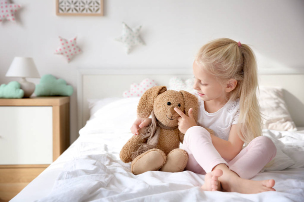 Cute little girl hugging toy bunny on bed at home - Fotó, kép