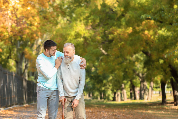 Young caregiver walking with senior man in park - Valokuva, kuva