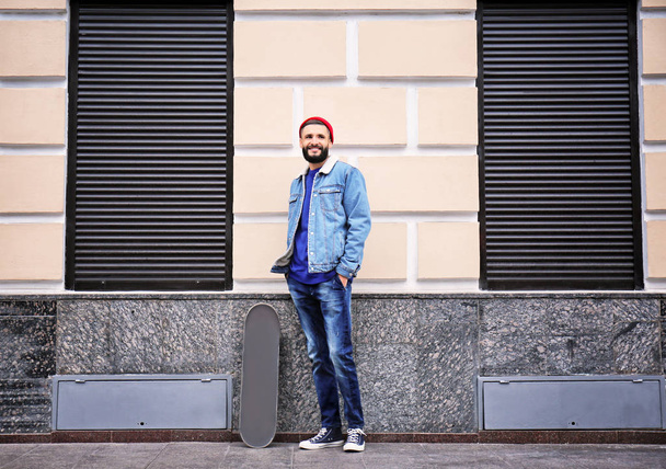 Attractive young hipster with skateboard on city street - Foto, Bild