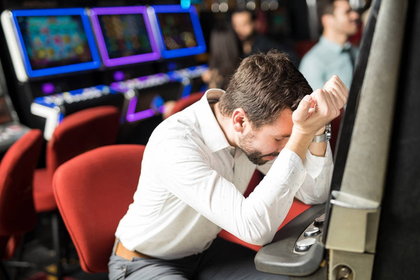 Unlucky young man feeling sad and stressed after losing his money playing slots in a casino - Photo, image