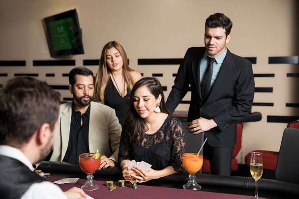 Hezká mladá žena hraje rukou dobrý poker v kasinu, zatímco její přátelé stát vedle ní a podporovat ji - Fotografie, Obrázek
