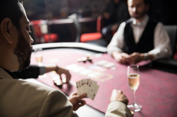 Sicht eines jungen Mannes in einem Anzug, der während eines Pokerspiels in einem Casino eine Wette abschließt - Foto, Bild